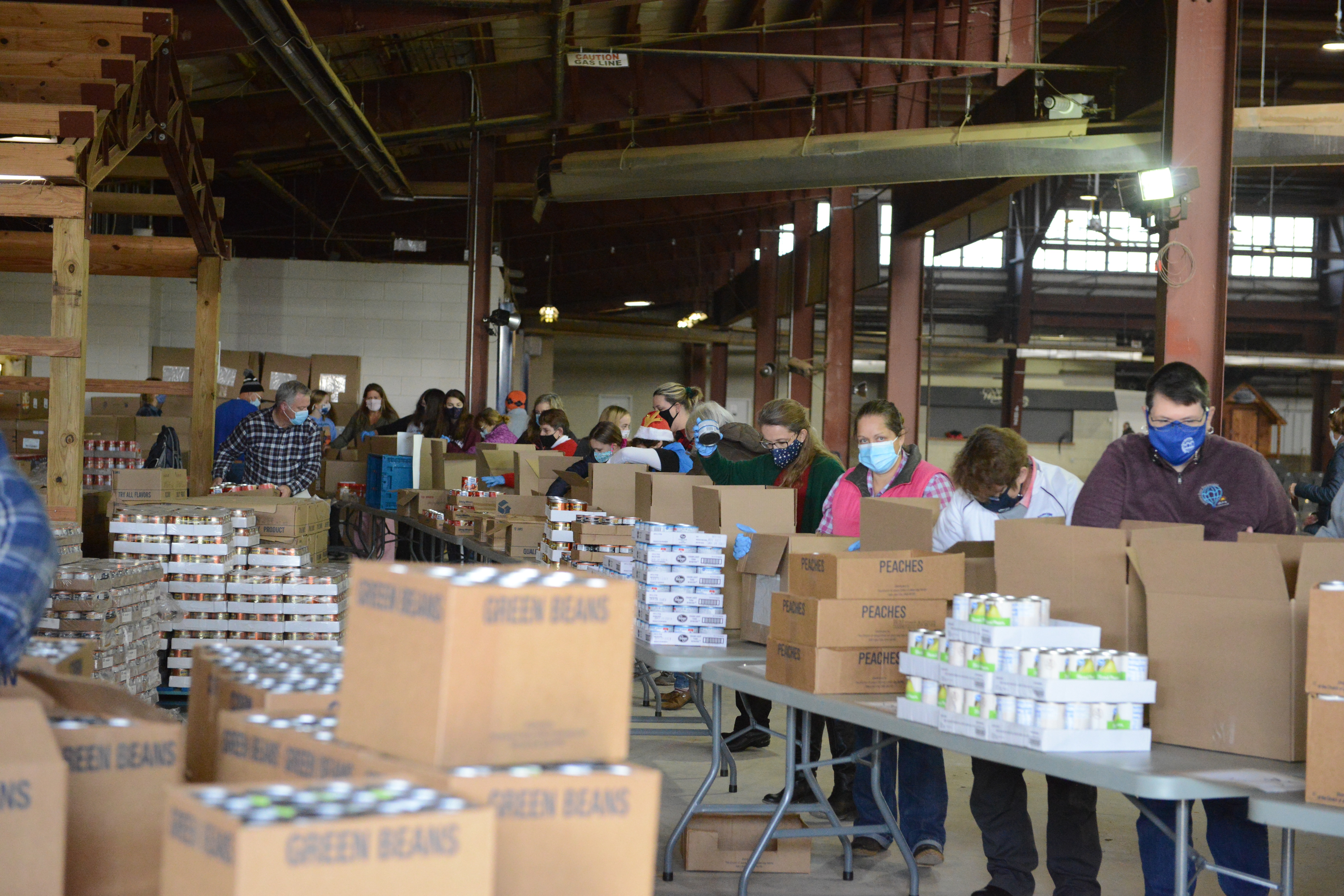 Long line of volunteers, all wearing masks, busy packing boxes with canned food items.